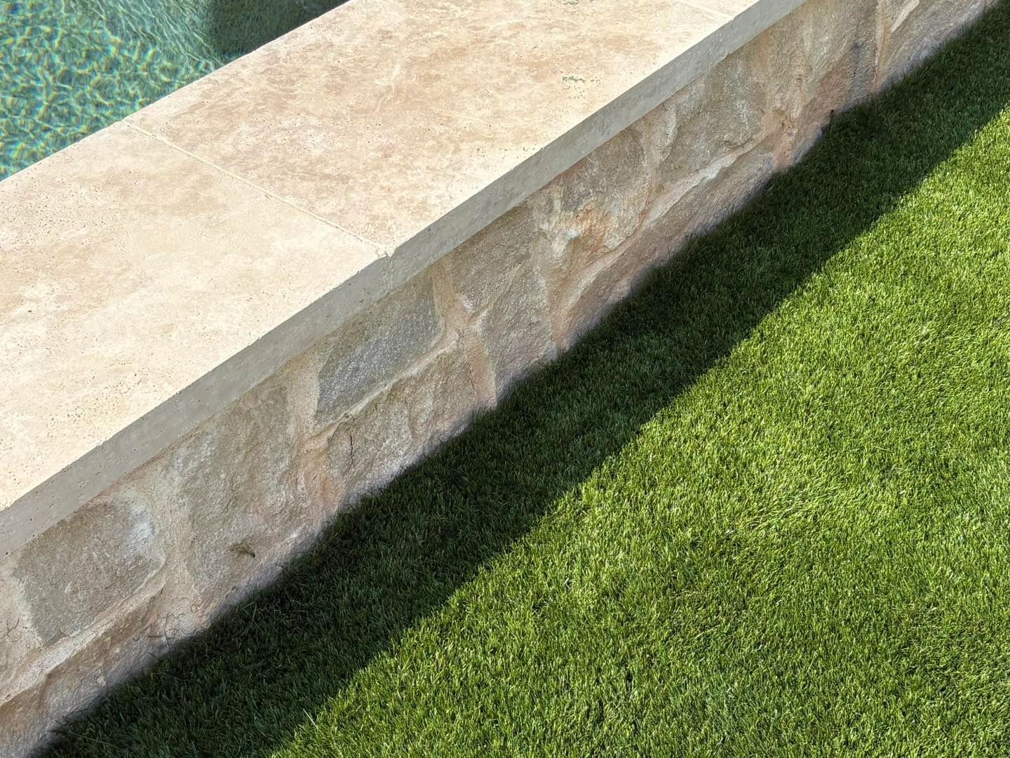 Artificial turf meeting natural stone pool coping, clean edge detail