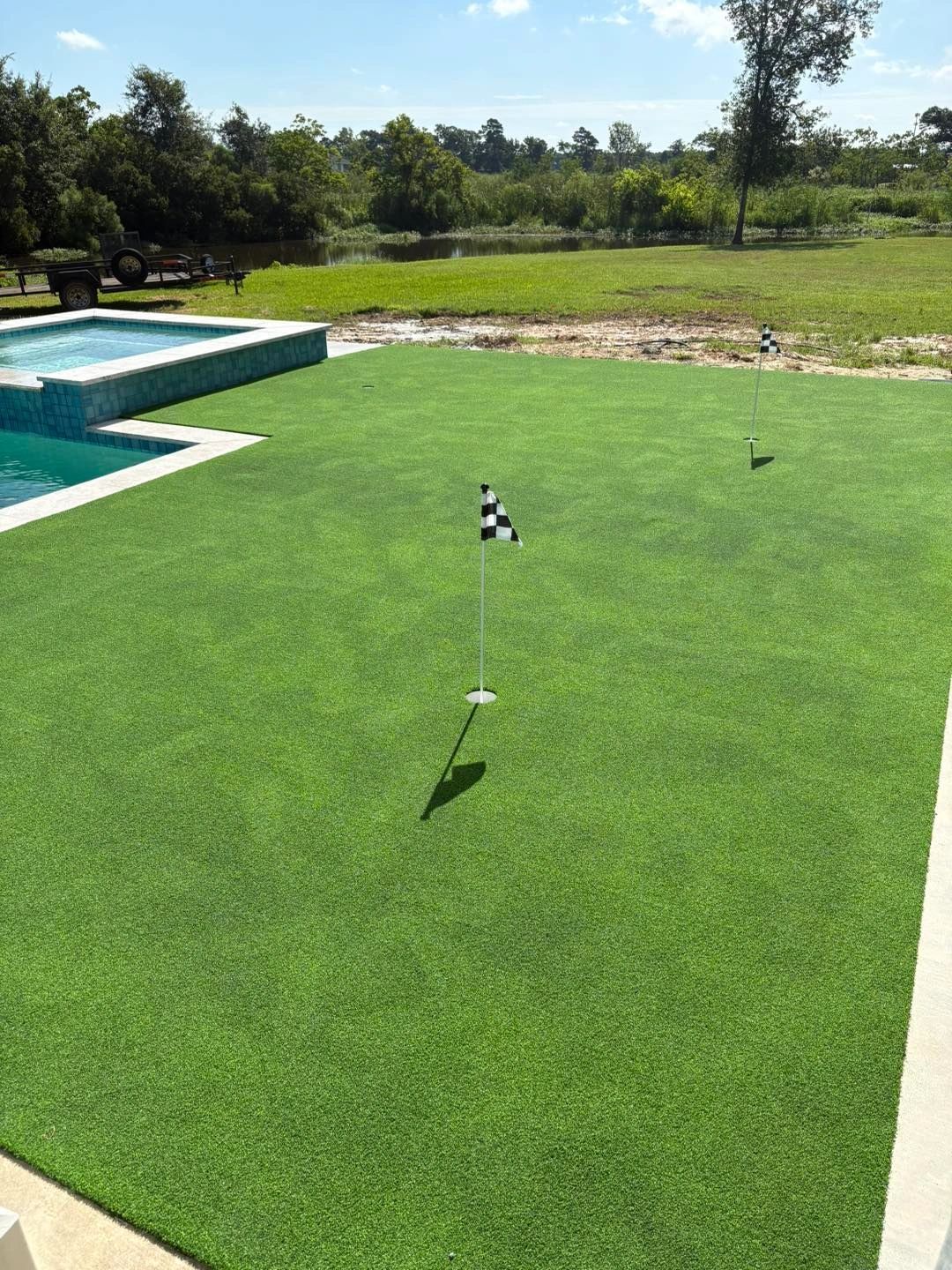 Backyard putting green with checkered flags beside pool