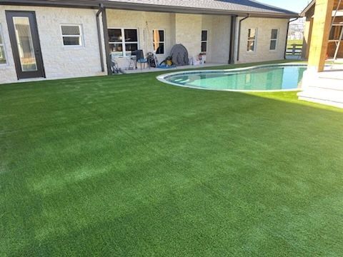 Backyard turf wrapping around curved pool and stone house