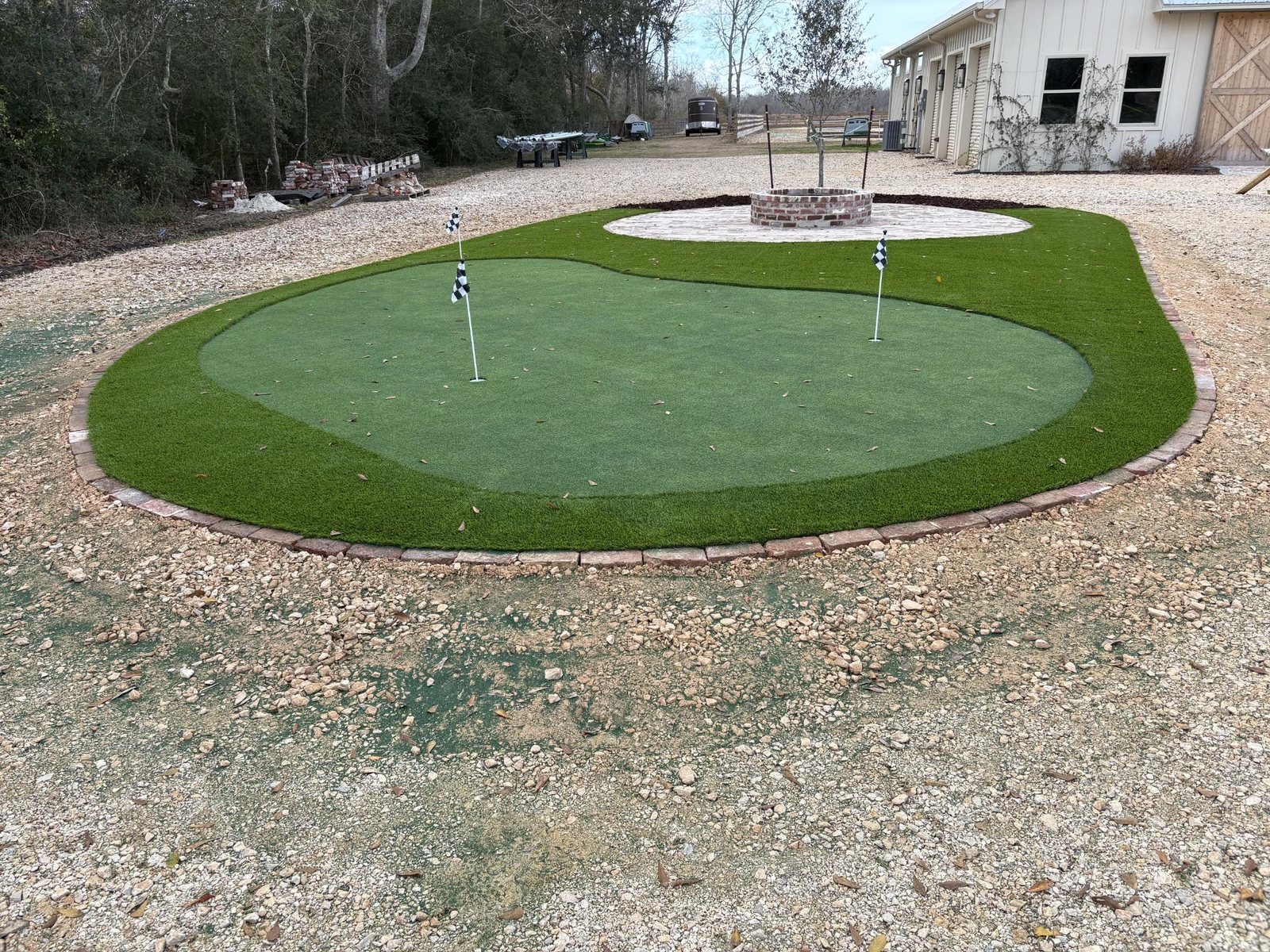 Wide view of custom putting green with brick edging in front of country barn