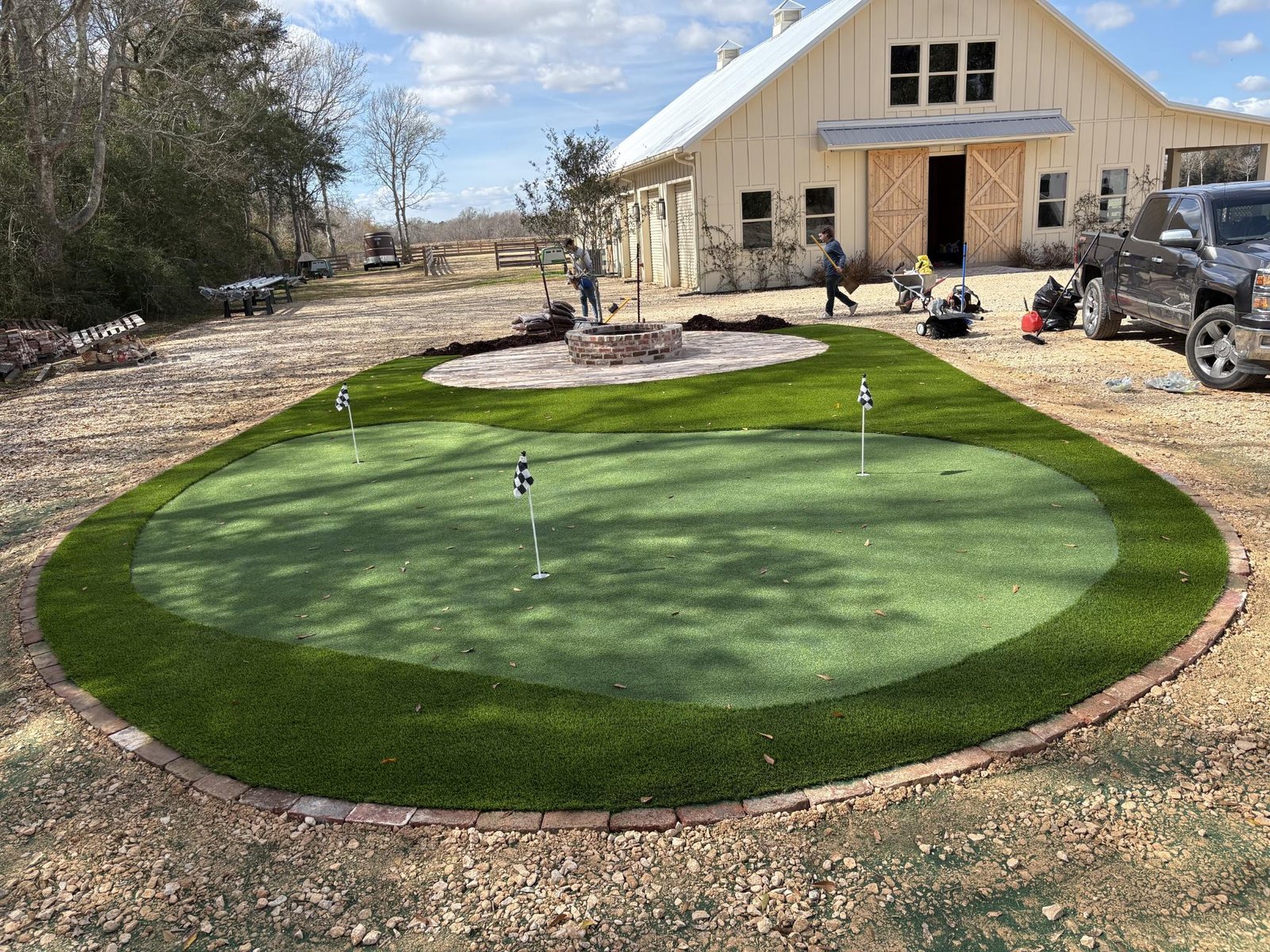 Custom putting green with fire pit and brick border at country barn